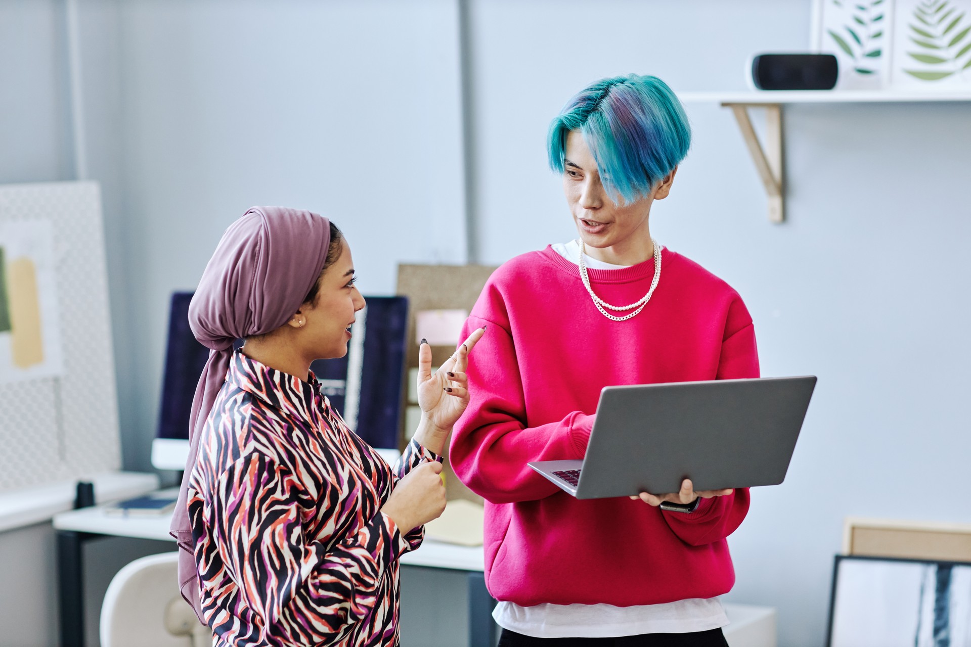 Creative gen Z team discussing project standing in office and holding laptop